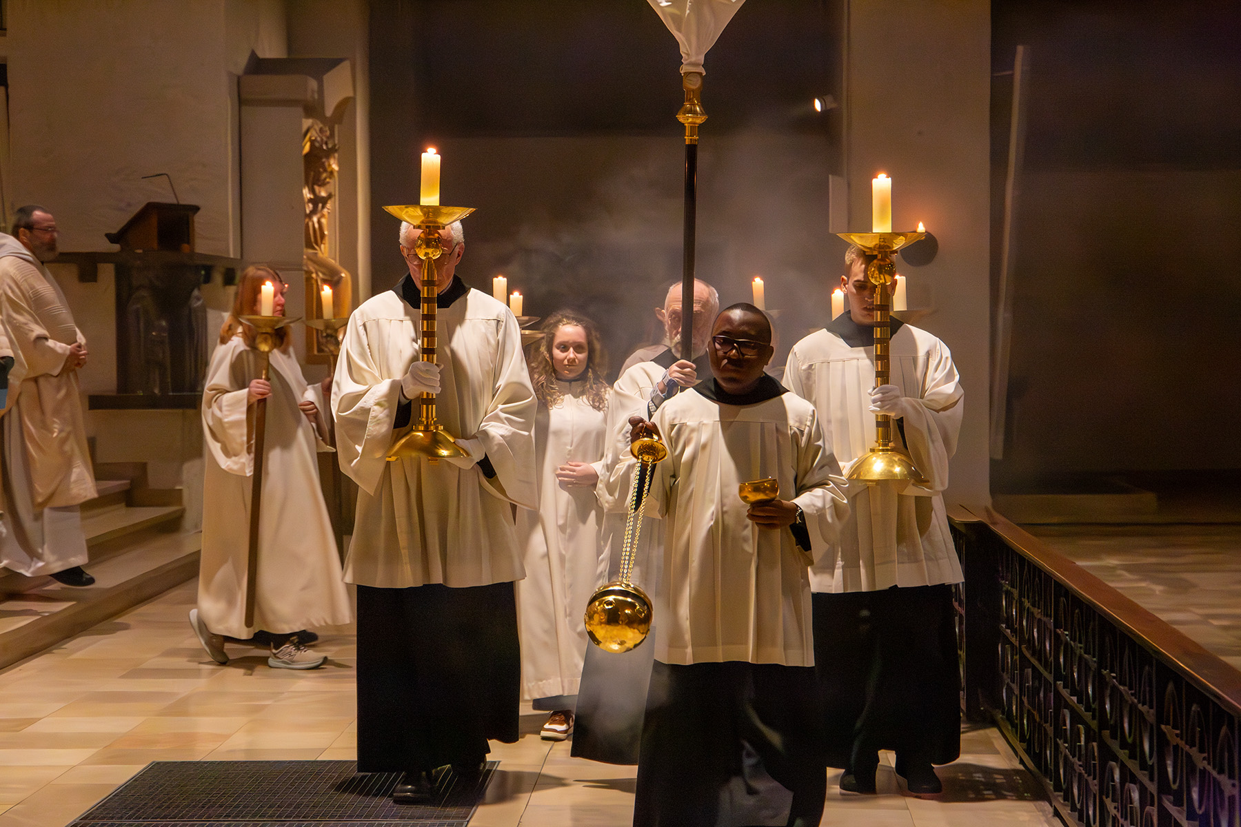 Menschen ziehen mit Kerzen und Weihrauch durch die Kirche