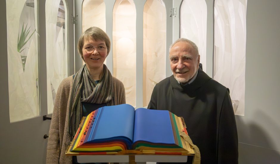 Frau und Mann stehen hinter einem bunt bemalten Buch